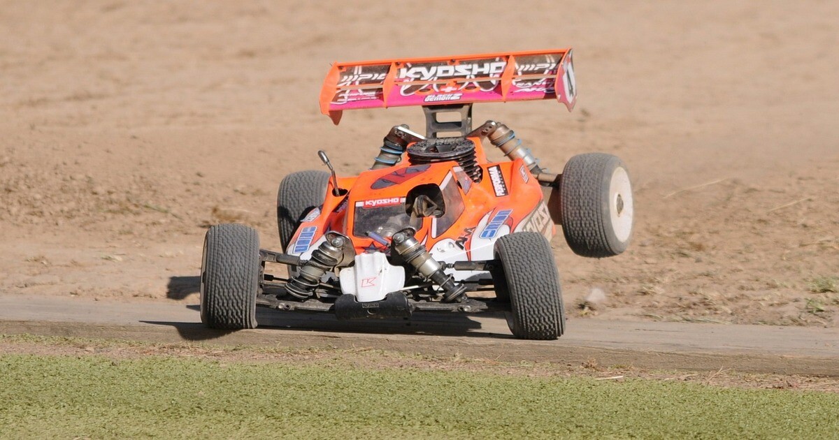 An RC buggy being driven on a grass and dirt track.